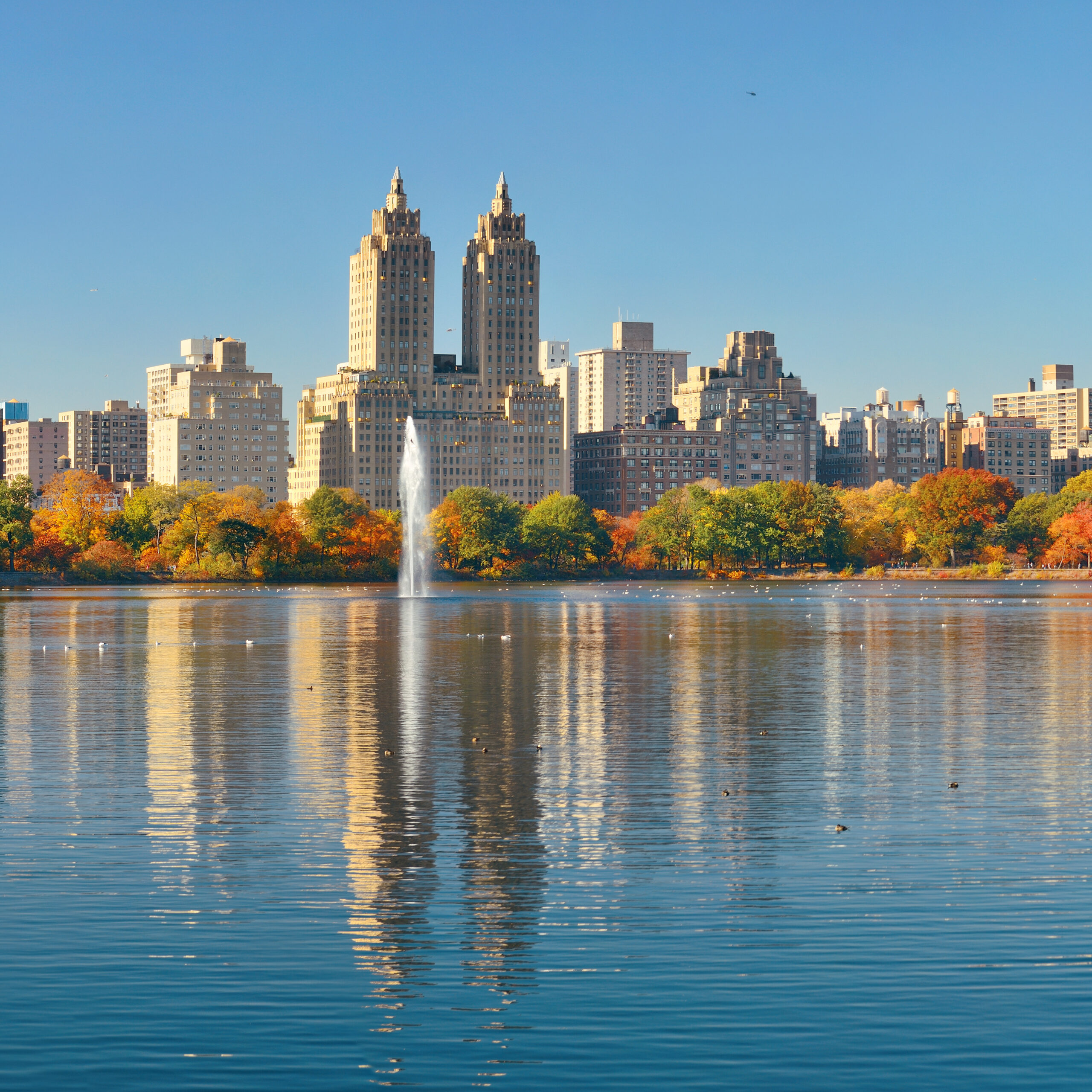 Central Park lake reflecting twin towers amid fall foliage