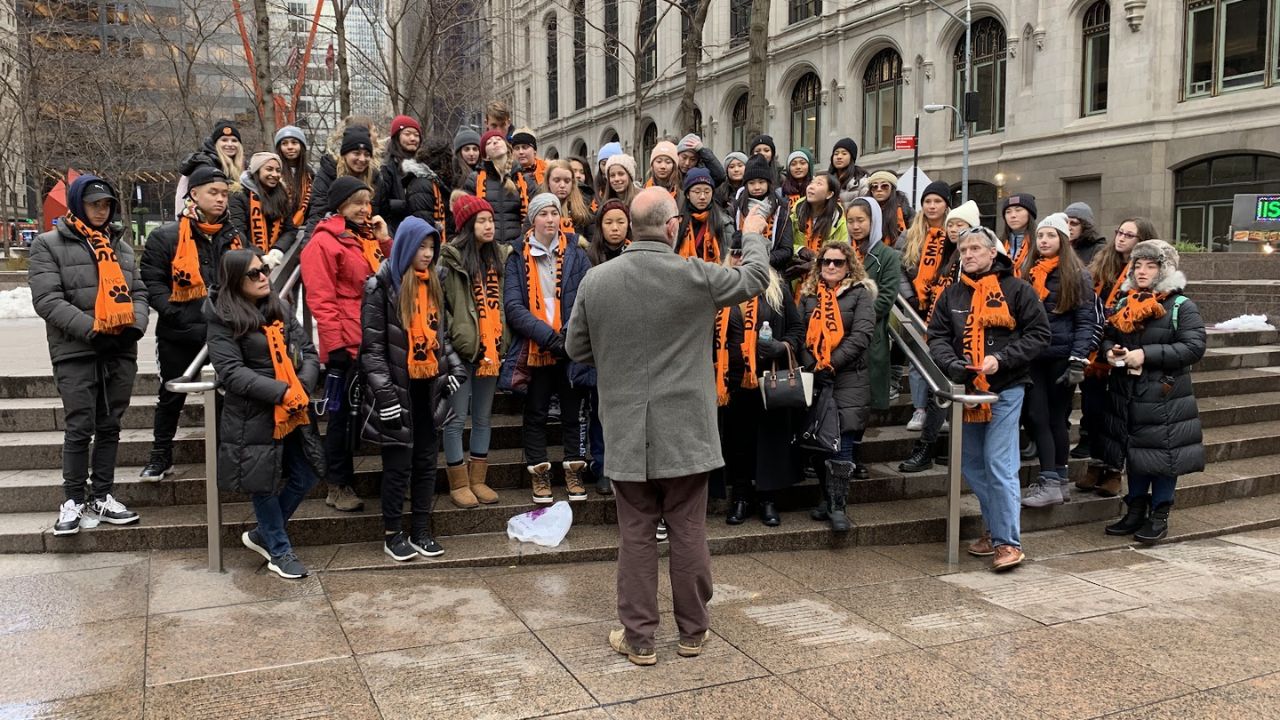Group in orange scarves gathers for historical city tour outdoors.
