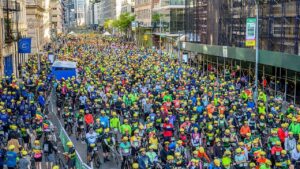 Massive crowd of cyclists in colorful gear and yellow helmets participating in TD Five Boro Bike Tour in New York City.