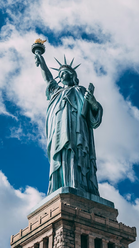 Statue of Liberty viewed from below against cloudy sky.
