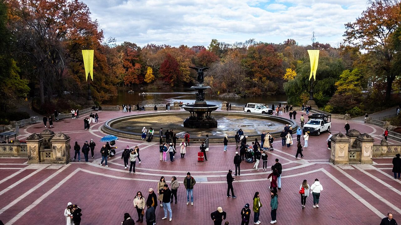 Bethesda Terrace fountain with autumn trees and visitors.