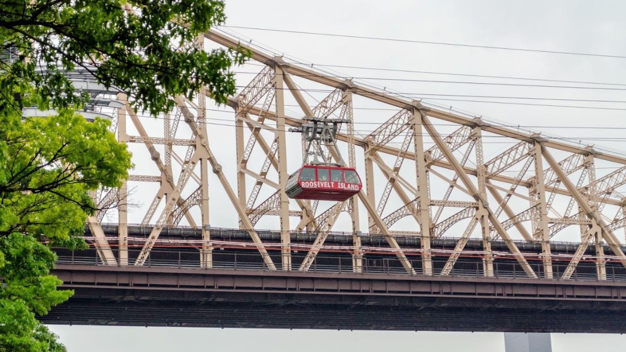  Roosevelt Island Tramway passing Queensboro Bridge with city skyline.
