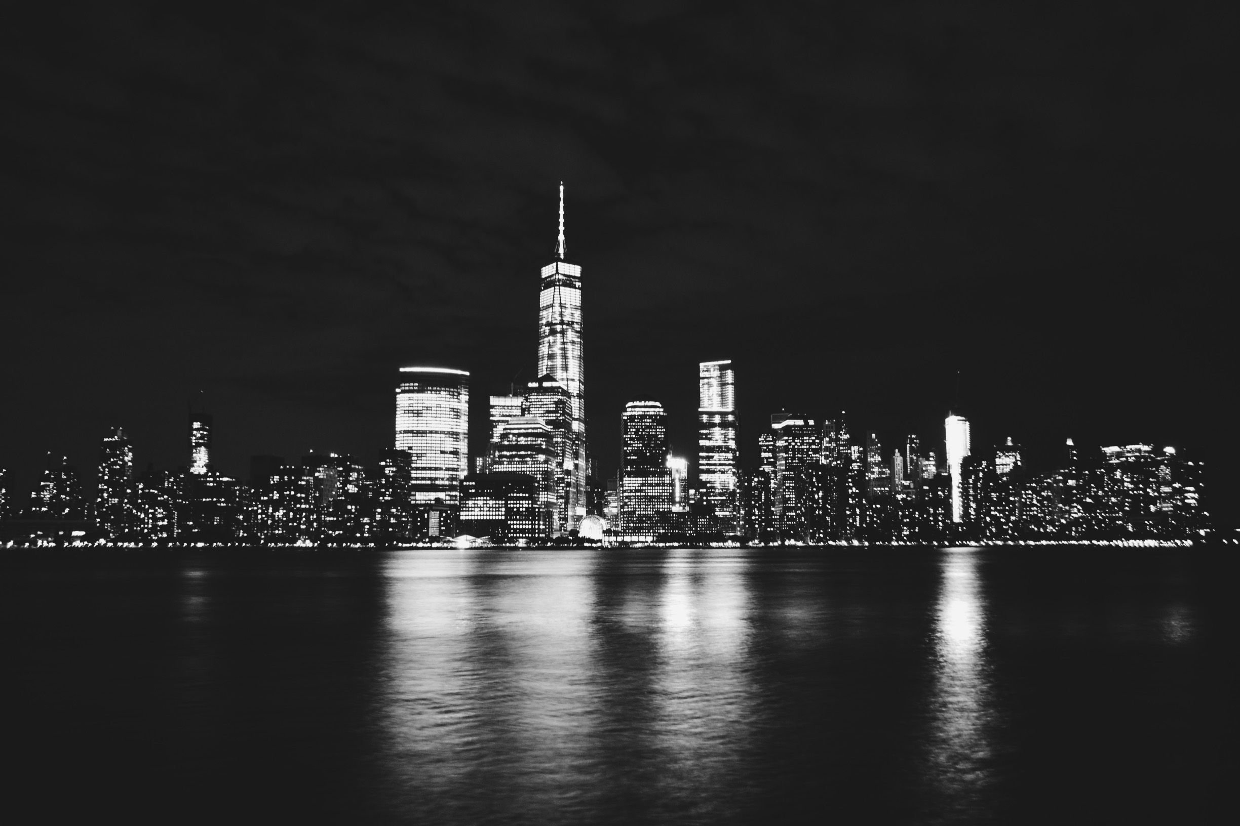Group of students walking along a NYC waterfront at night, relaxing and taking photos of the glowing skyline while city lights reflect across the water.