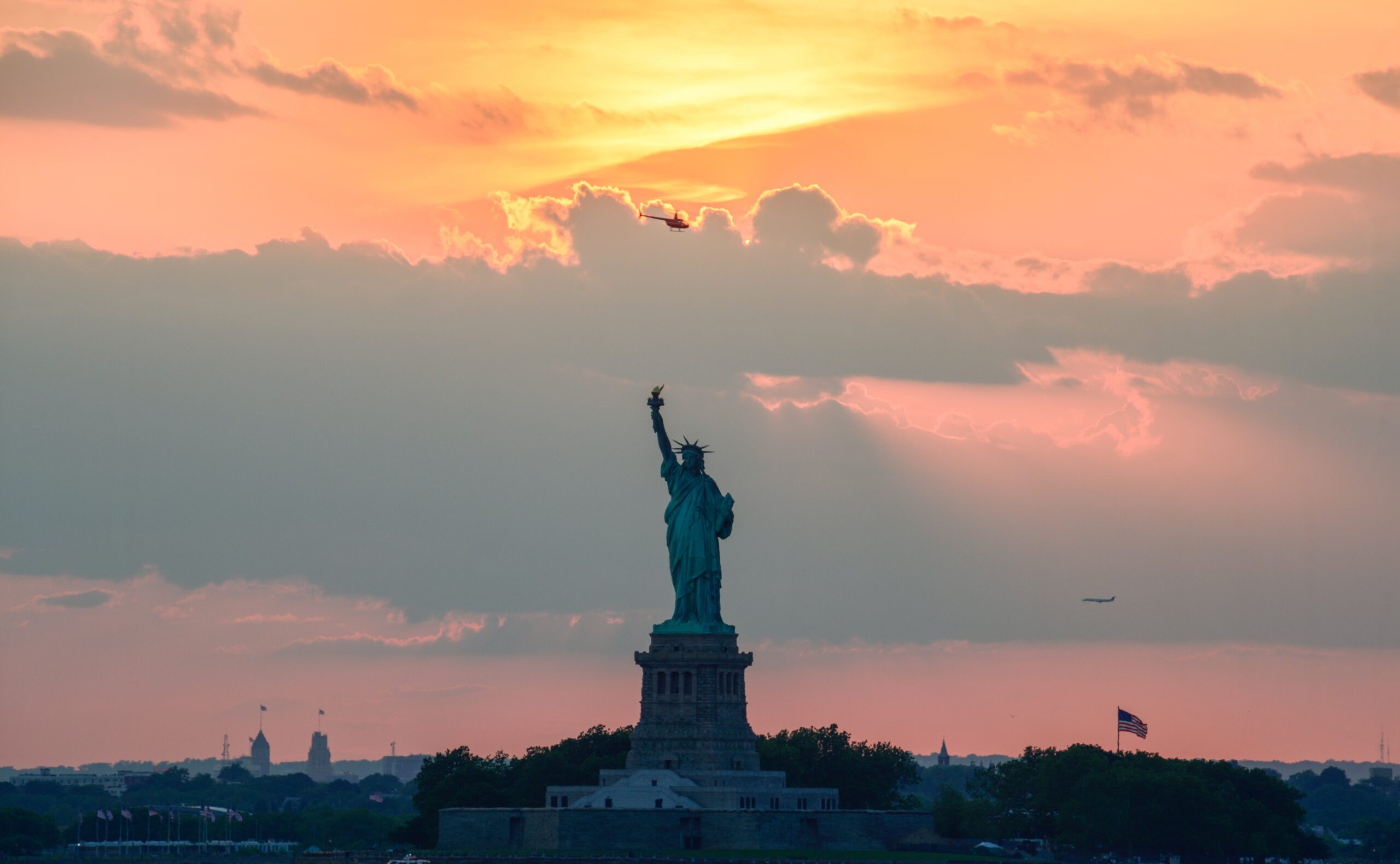 Statue of Liberty during sunset with golden light reflecting across New York Harbor and the Manhattan skyline glowing softly in the background.