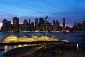 Brooklyn Heights streets glowing under warm streetlights with the Manhattan skyline shining across the river at night.