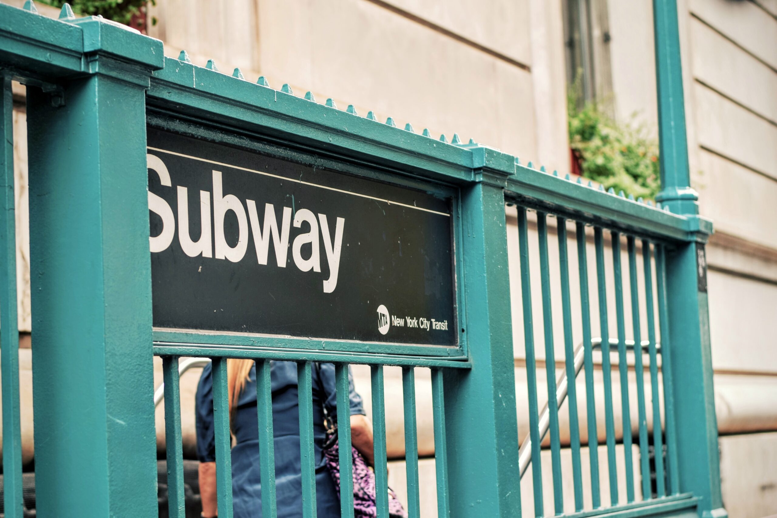 Close-up of a teal MTA New York City Transit subway entrance sign on an iron railing