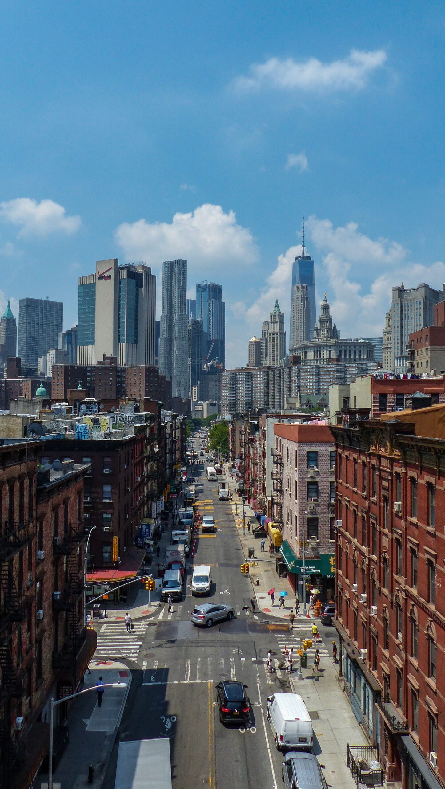 Top aerial view of Manhattan showing busy roads, moving cars, yellow taxis, tall buildings, and crowded city blocks stretching across the urban skyline.