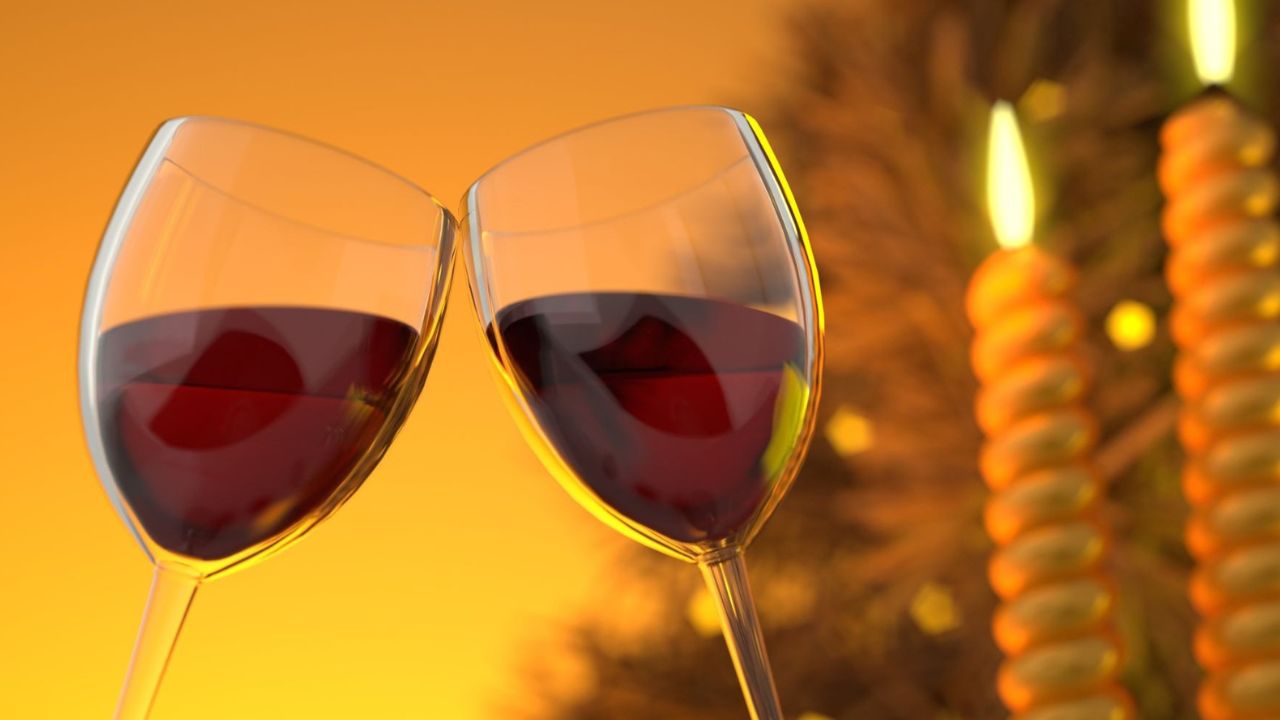 Two red wine glasses clinking with candles in background