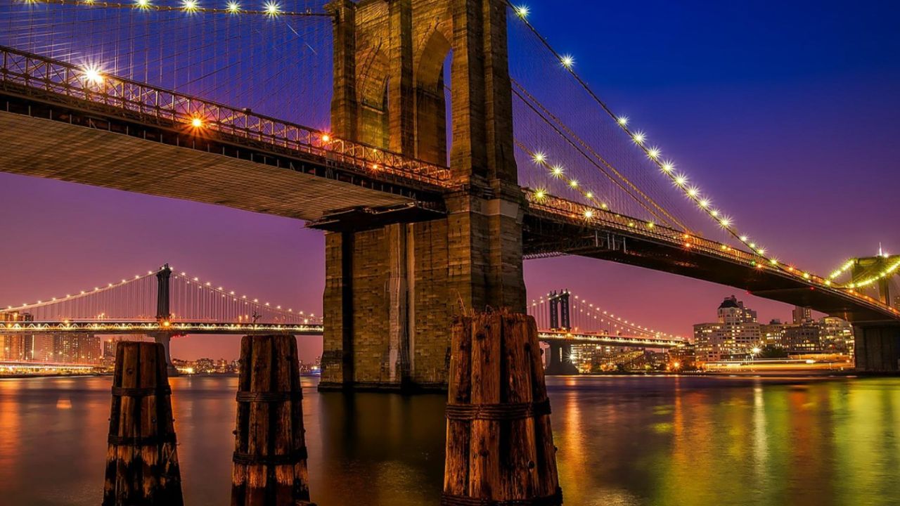 Brooklyn Bridge glowing over East River at twilight night