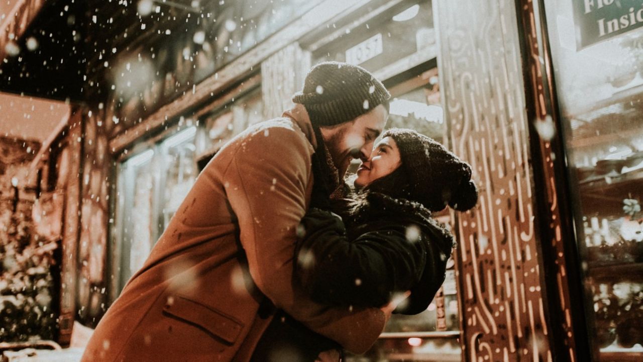 Couple embracing romantically outside flower shop in falling snow.
