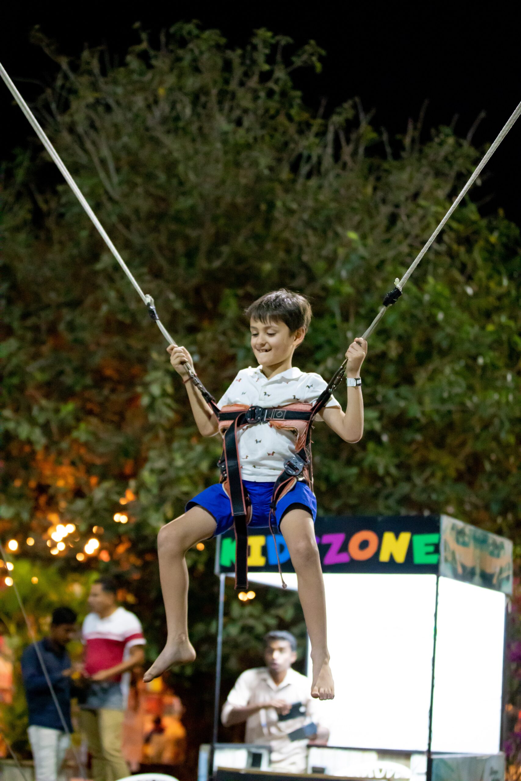 Boy in harness jumping on bungee trampoline outdoors