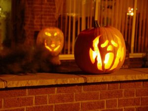 Carved jack-o'-lanterns — Two glowing jack-o'-lanterns on brick porch ledge