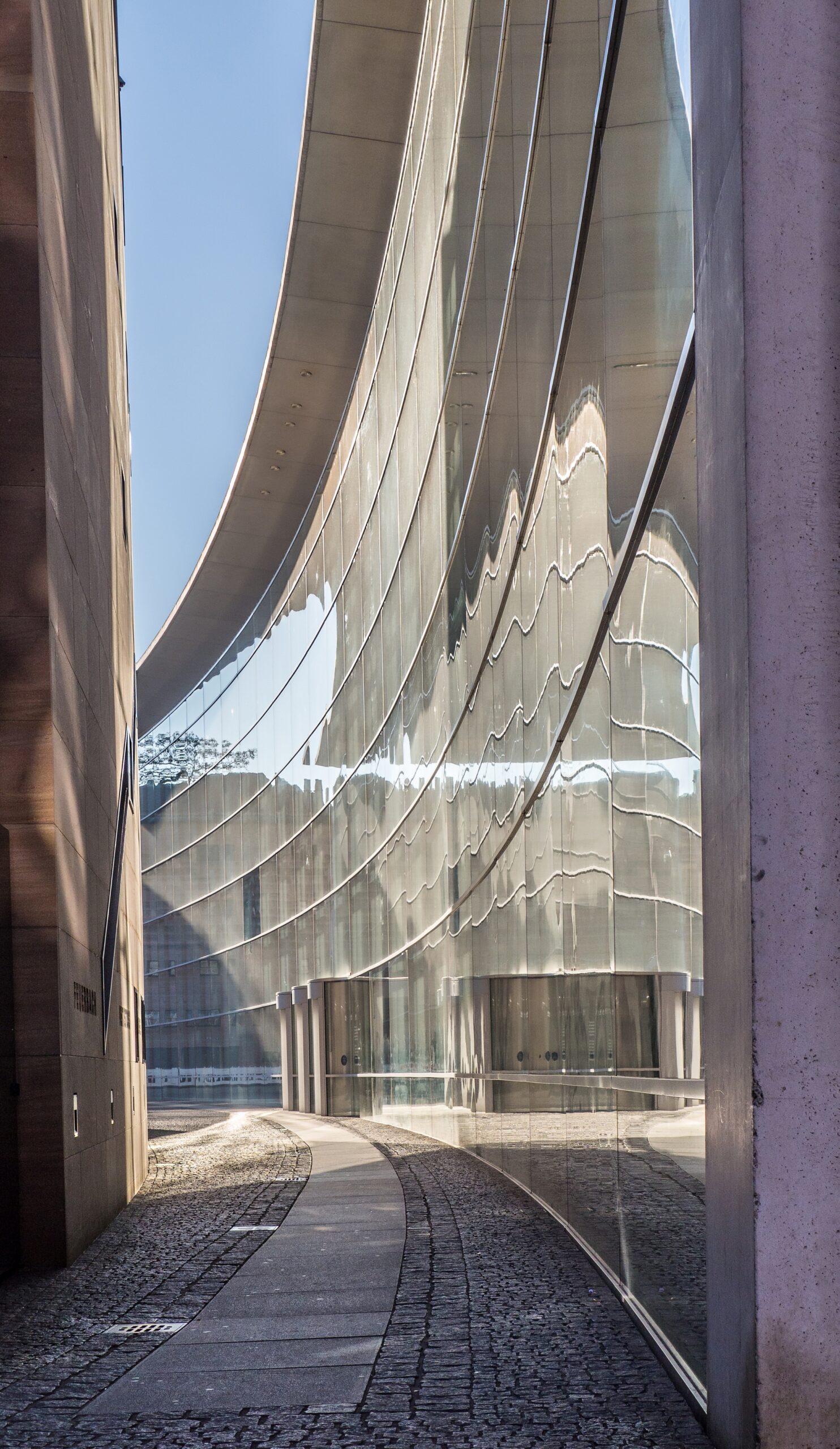 Curved glass museum of modern art facade reflecting pathway and sky