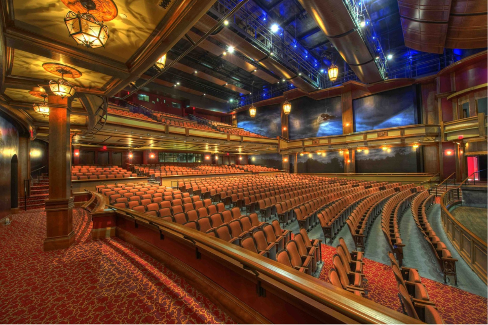 Empty theater auditorium with red seats and balcony levels.
