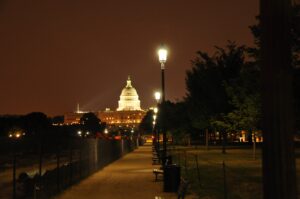U.S. Capitol dome illuminated at night, tree-lined path