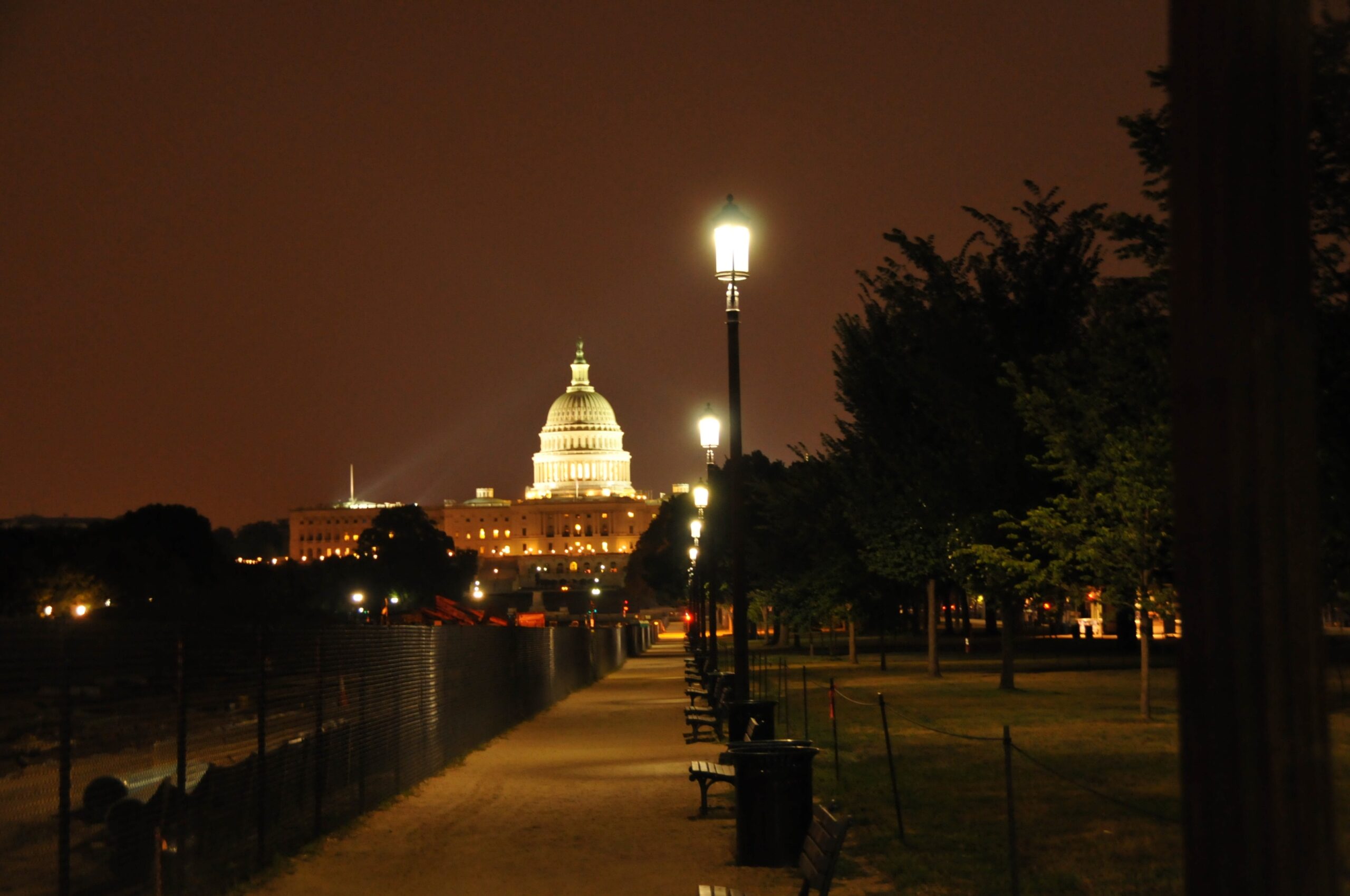 U.S. Capitol dome illuminated at night, tree-lined path