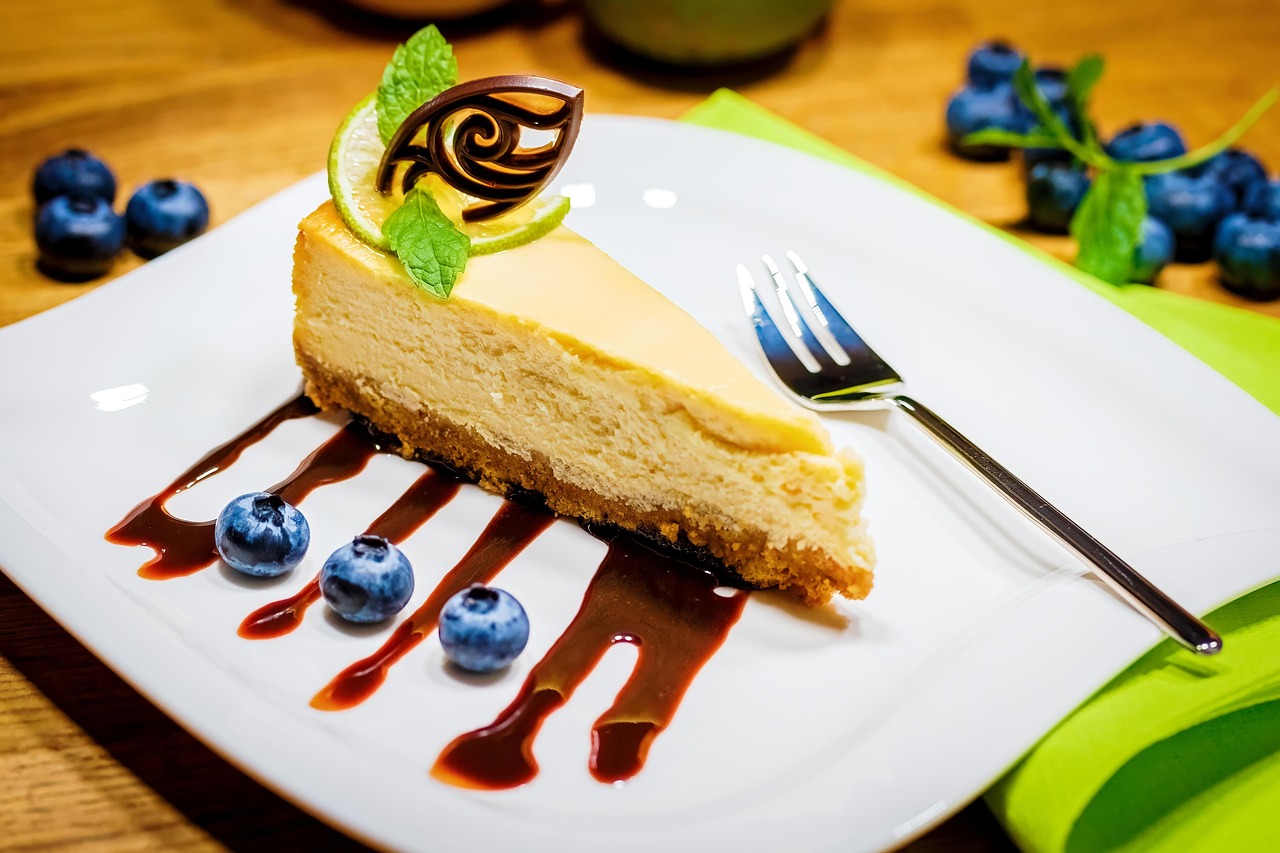 Cheesecake slice plated with blueberries and chocolate garnish.