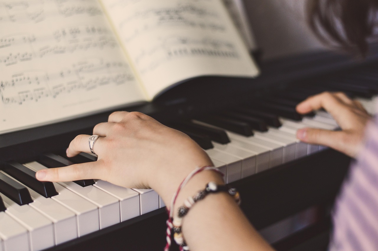 Close-up of hands playing piano from sheet music.