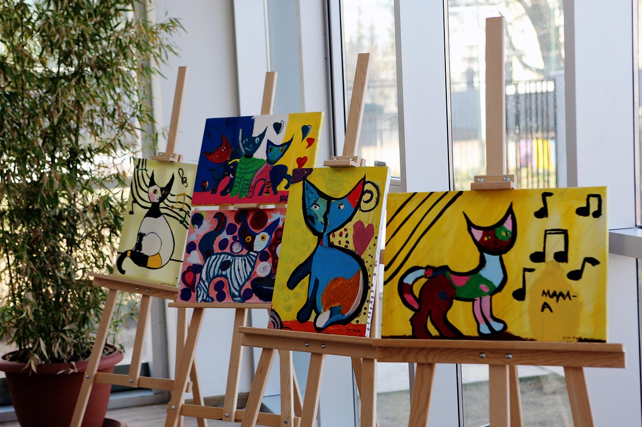 Colorful cat paintings displayed on easels indoors.