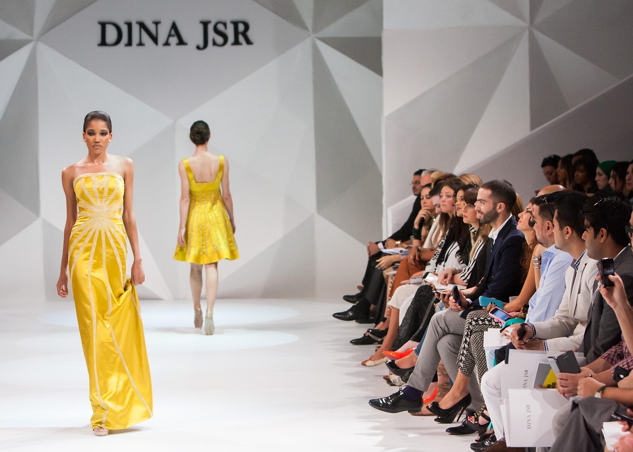 Fashion models in yellow gowns walk a runway show.