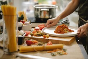 Hands plating spaghetti with sauce in a kitchen.