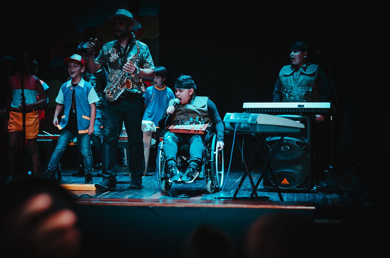 Musicians performing on stage; boy sings into microphone, wheelchair.