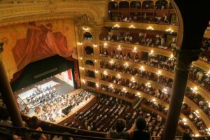 Ornate opera house interior, orchestra performing before full audience.