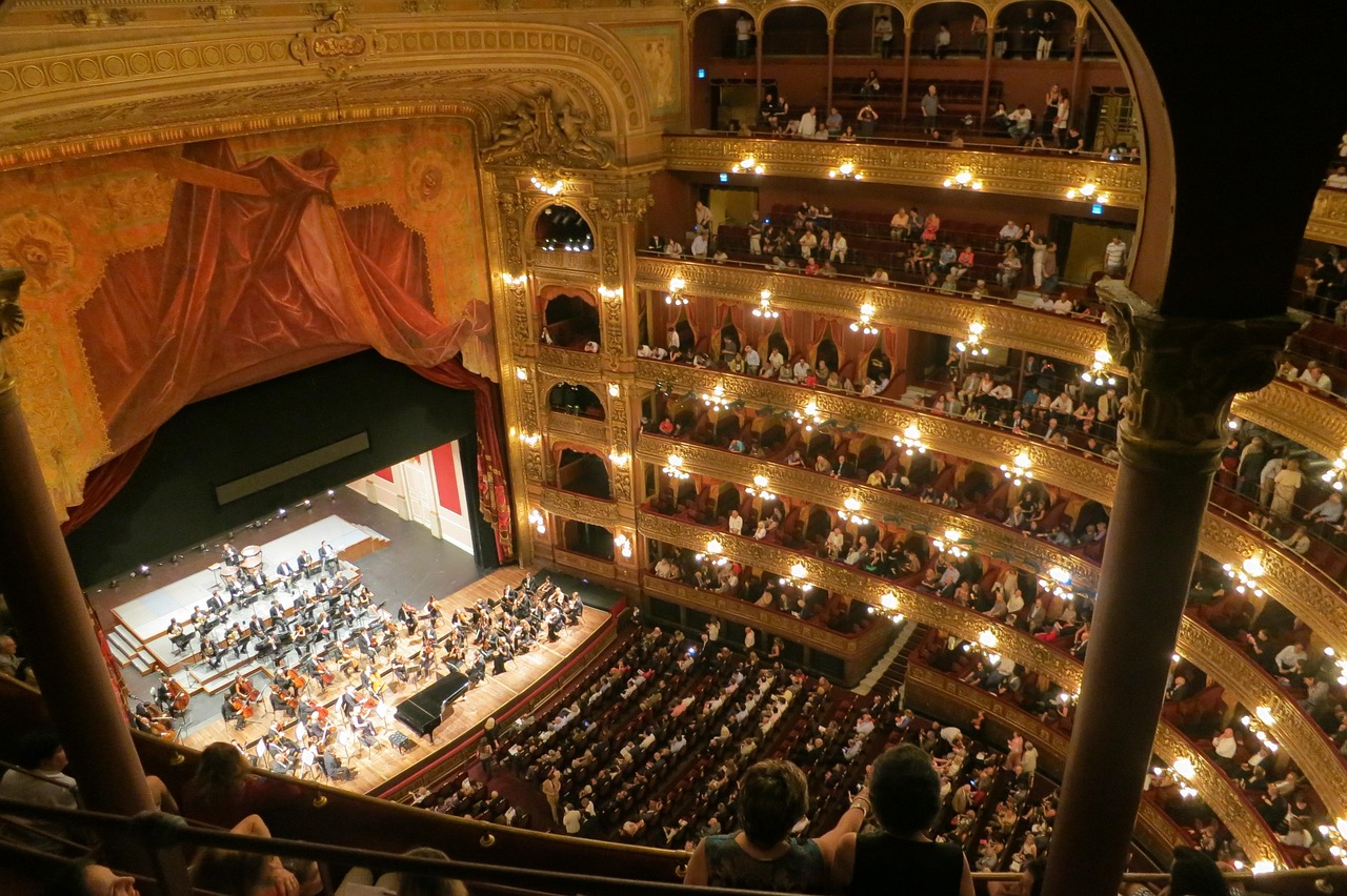 Ornate opera house interior, orchestra performing before full audience.